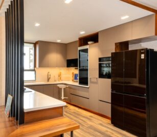Modern U-shaped modular kitchen with grey cabinets, integrated appliances, black refrigerator, and wood accents on flooring and counter