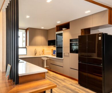 Modern U-shaped modular kitchen with grey cabinets, integrated appliances, black refrigerator, and wood accents on flooring and counter